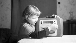 Ein Mädchen sitzt an einem Tisch und spielt am Kofferradio "Libelle".