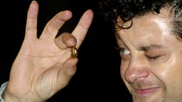 Archivaufnahme: Andy Serkis fixiert bei der Filmpremiere von "Herr der Ringe: Die Rückkehr des Königs" 2013 mit einem Augen einen goldenen Ring in seiner Hand.