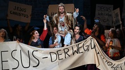 Szenenfoto: Schauspieler Andreas Bongard als Jesus von Nazareth, der von Menschen auf den Schultern getragen wird.