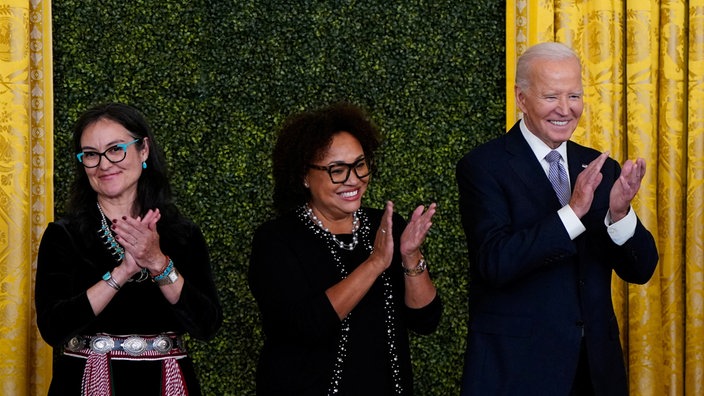 US-Präsident Joe Biden applaudiert zusammen Maria Jackson und Shelly Lowe auf einer Bühen im Weißen Haus.