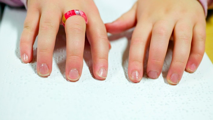 Die Hände eines Mädchens beim Lesen der Braille-Schrift