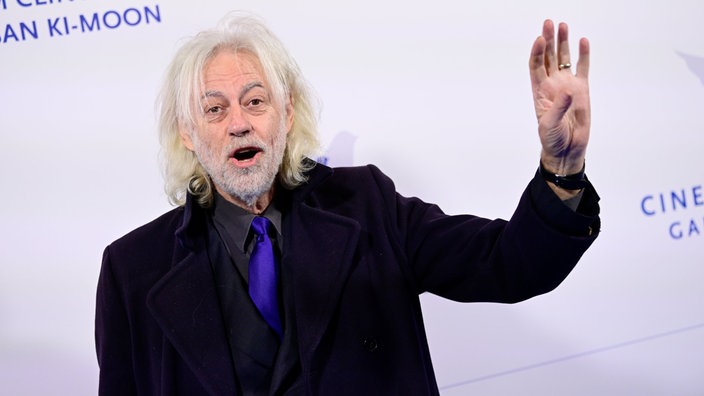 Geldof kommt zur Cinema for Peace Gala Berlin am 19.02.2024. Er winkt mit dem linken Arm.