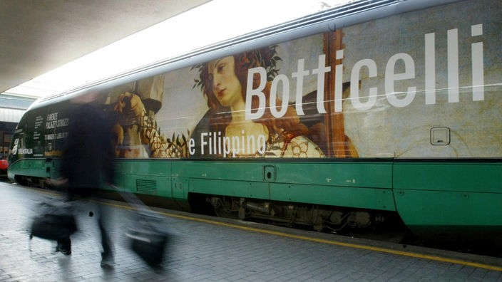 Eine Person läuft an einem Zug vorbei, auf dem Werbung für die Botticelli-Schau 2016 in Florenz abgebildet ist.