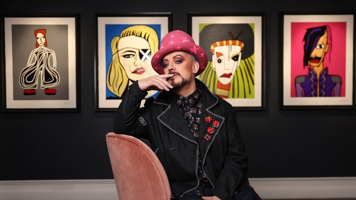 Boy George posiert vor seinen Gemälden verschiedener Popstars.