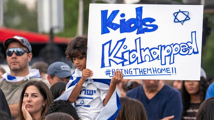 Ein Junge hält während einer Demonstration ein Schild mit der Aufschrift Schild mit der Aufschrift "Kids Kidnapped BringThemHome"