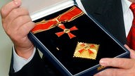 Ein Bundesverdienstkreuz wird in seiner Fassung von zwei Händen gehalten. 