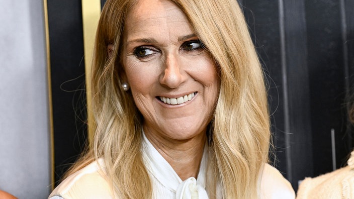 Céline Dion in weißer Bluse schaut am 17.06.2024 lächelnd zur Seite.