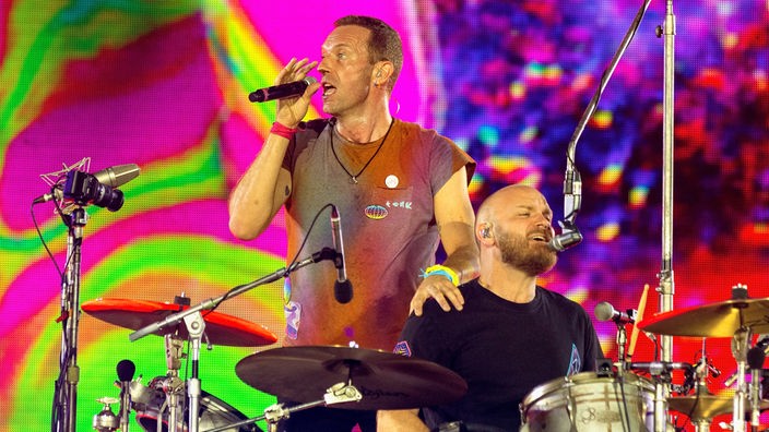 Chris Martin (l), Sänger von Coldplay, steht neben Will Champion, dem Schlagzeuger der Band, während der "Music of the Spheres"-Tour auf der Bühne