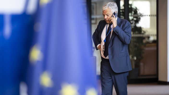 Reynders telefoniert im Gehen mit seinem Handy am 25.06.2024. Im Vordergrund hängt die EU-Flagge.