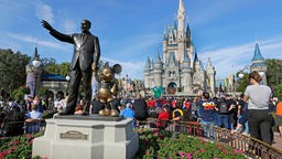 Statue von Walt Disney und Mickey Mouse im Vordergrund. Im Hintergrund Touristen vor dem Cinderella Castle