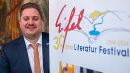 Johannes Zierden steht am 03.11.2023 hinter einem Plakat mit der Aufschrift: "30 Jahre Eifel Literatur Festival