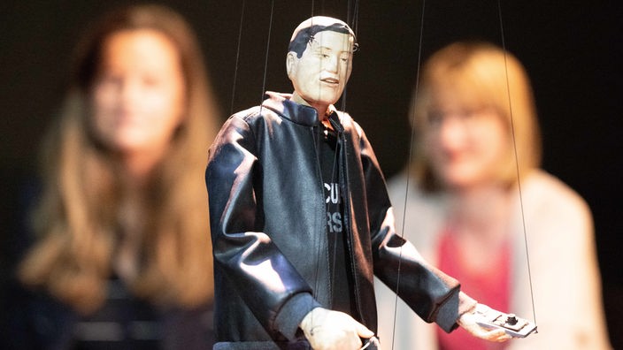 Teilnehmer einer Pressekonferenz begutachten eine aus Birnenholz geschaffene Marionette von US-Tech-Milliardär Elon Musk.
