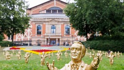 25.07.2023, Bayern, Bayreuth: Goldfarbene Wagner-Figuren des Konzeptkünstler Ottmar Hörl stehen im Rahmen der Kunstinstallation "You're welcome" vor dem Festspielhaus vor Beginn der Bayreuther Festspiele.