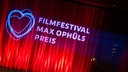 Archivaufnahme von 2023: Eine roter Vorhang auf den Logo und Schriftzug vom "Filmfestival Max Ophüls Preis" projiziert werden.