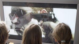 Drei Kinder schauen sich auf einem Bildschirm eine gewalttätige Szene an.