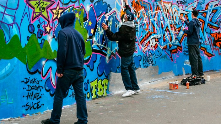 Drei junge Männer sprayen Graffitis an eine Betonwand