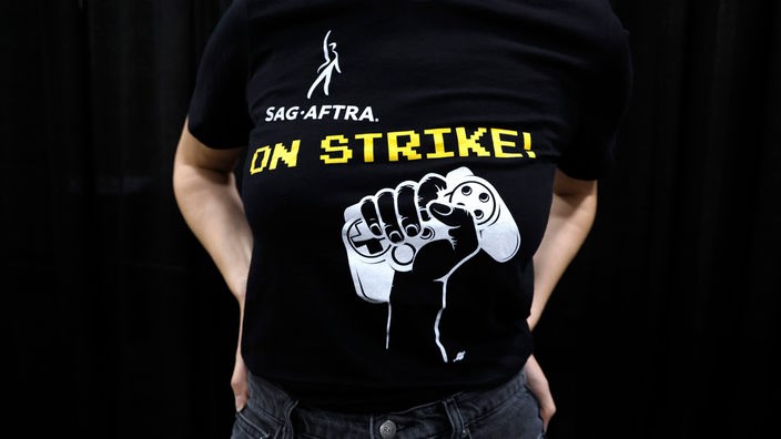 Symbolbild: T-Shirt der Gewerkschaft der SAG-Aftra, mit dem Aufdruck "On Strike" neben einem Game-Controller in einer Faust.