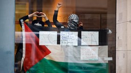Demonstranten mit einer Palästina-Fahne hinter einer Glasscheibe im Innenhof des Gebäudes der Sozialwissenschaften an der Berliner Humboldt-Universität.