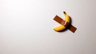 Eine Banane klebt mit Klebeband an der Wand.