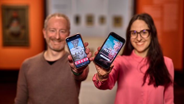 Zwei Menschen zeigen die "It's an art match" App auf ihrem Smartphone.