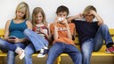 Vier Jugendliche sitzen auf einer Bank und nutzen ihre Handys