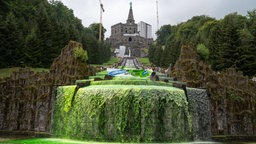 Von Umweltaktivisten grün gefärbtes Wasser läuft die Stufen der Kasseler Wasserspiele herunter, darüber ein Transparent.