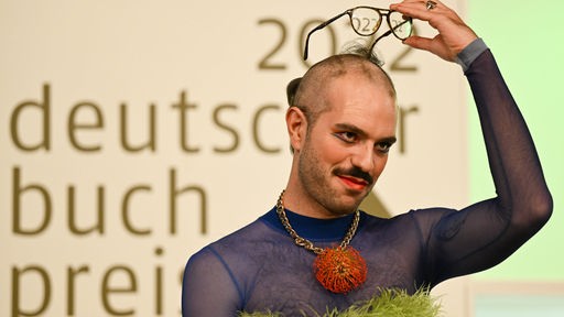 Kim de l'Horizon ("Blutbuch") hat sich nach seiner Auszeichnung mit dem Deutschen Buchpreises 2022 die Haare abrasiert aus Solidarität mit den Frauen im Iran den Kopf rasiert.