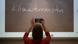 ine Journalistin fotografiert mit ihrem Smartphone das «Unwort des Jahres» 2022, «Klimaterroristen», das während seiner Bekanntgabe an der Philipps-Universit·t an eine Wand projiziert wird.