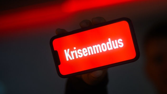 Krisenmodus steht in weißer Schrift vor rotem Hintergrund auf einem Smarphone-Display.