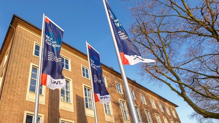 Drei Fahnen mit dem LWL-Logo wehen an Masten vor dem LWL-Landeshaus