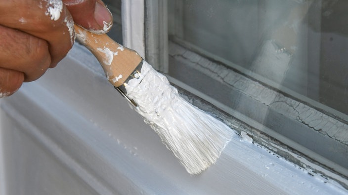 Ein Maler streicht mit einem Pinsel einen alten Fensterrahmen.