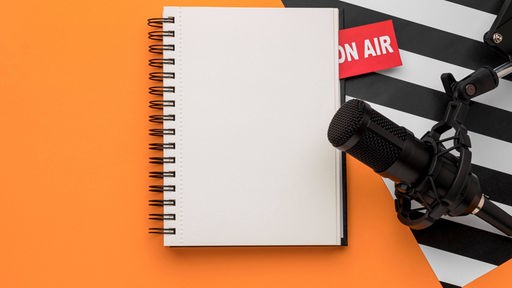 Ein leerer Notizblock und ein Mikrofon liegen über einem "On air"-Schild.