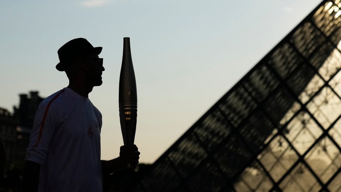 Der französische Fotograf JR (Jean-René) hält die olympische Fackel 14.07.2024 im Hof des Louvre-Museums.