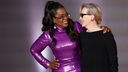 Oprah Winfrey und Merly Streep haben ihre Arme umeinander gelegt und lächeln sich an.