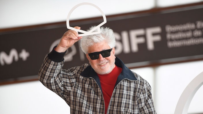 Almodóvar hält sich das Logo des Filmfestivals auf den Kopf und lächelt.