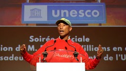 Pharrell Williams spricht in ein Mikrofon, im Hintergrund der Schriftzug der UNESCO.