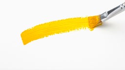 Ein Pinsel zieht einen gelben Strich auf ein weißes Papier.