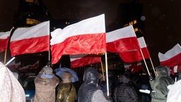 Menschen schwenken die polnische Nationalflagge bei einer Demonstration vor dem Hauptsitz des staatlichen Fernsehsenders TVP in Warschau, Polen.
