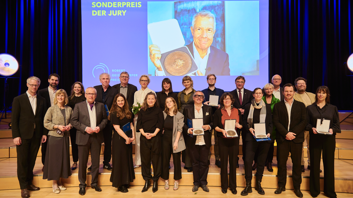 Gruppenbild der Preisträger am 8. Oktober 2024 beim Norddeutschen Rundfunk (NDR) in Hamburg mit Peter Klöppel auf einem großen Bildschirm im Hintrgrund.