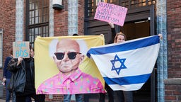 Protestierende halten vor dem Eingang der Hochschule für bildende Künste Hamburg (HfbK) Tranparente mit der Aufschrift "Ruangrupa C$sh From Anti-semitism", "Fight BDS", eine Israelfahne und ein Bild von David Ben-Gurion hoch