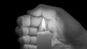 Eine Hand hält eine brennende Kerze vor schwarzem Hintergrund. 