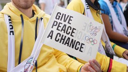 Auf einem Fähnchen des Turners Oleh Wernjajew aus der Ukraine steht: Give Peace a Chance