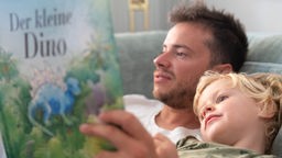 Vater liest seinem dreijährigem Sohn aus einem Dinosaurierbuch vor