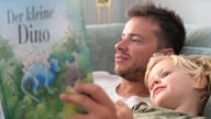 Vater liest seinem dreijährigem Sohn aus einem Dinosaurierbuch vor.