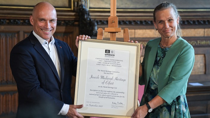 Andreas Horn (CDU), Oberbürgermeister der Stadt Erfurt, nimmt eine UNESCO-Urkunde von der Staatsministerin Katja Keul (Bündnis 90/Die Grünen) entgegen.