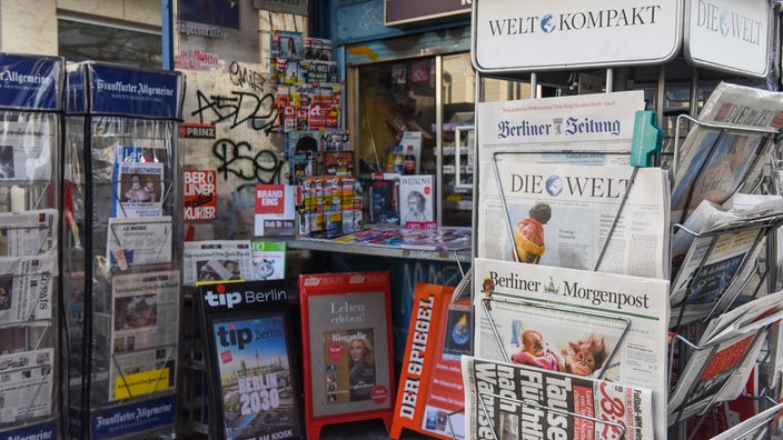 Ständer mit verschiedenen Zeitungen und Magazinen, aufgenommen 2015 vor einem Kiosk in Berlin.