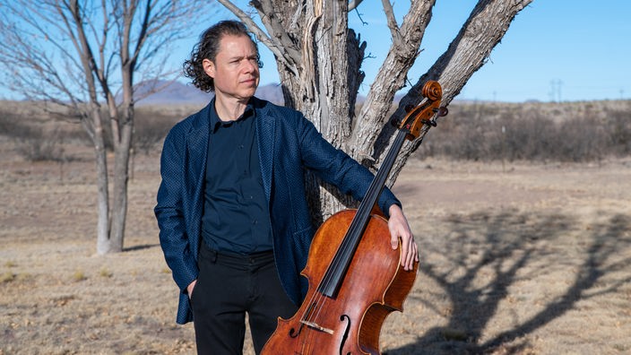 Der Cellist Matt Haimovitz steht mit seinem Cello vor einem Baum