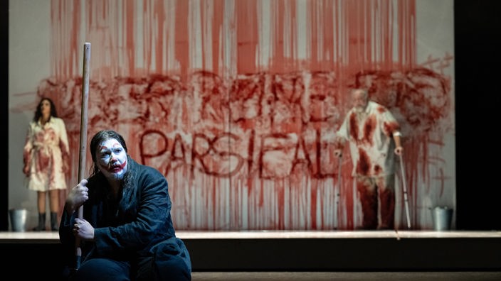 Daniel Frank (Parsifal), im Hintergrund: Sarah Ferede (Kundry), Hans-Peter König (Gurnemanz)