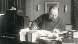 Schwarz-Weiß-Aufnahme von Jules Massenet bei der Arbeit am Schreibtisch.