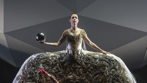 Lenneke Ruiten als Zauberin Alcina in der gleichnamigen Oper von Georg Friedrich Händel. Die Zauberin trägt ein ausgestelltes Kleid und hält eine Zauberkugel in der Hand.